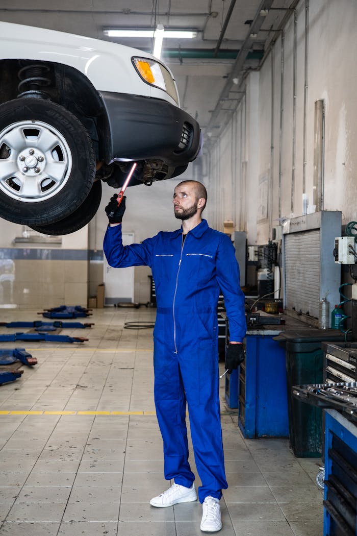creative-02 Mechanic in blue coverall inspecting car in auto repair shop. Professional vehicle maintenance in progress.